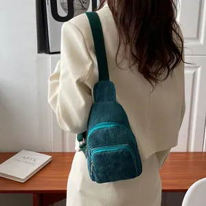 Detail view of a dark green corduroy crossbody bag worn over a white blazer