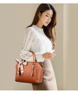 Detail view of brown crocodile texture handbag with decorative printed silk scarf and gold hardware