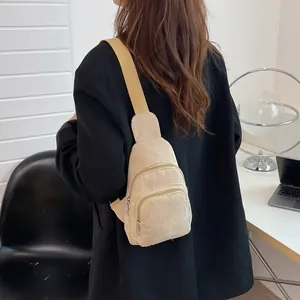 Detail view of beige corduroy crossbody bag with multiple zippers worn by model in room
