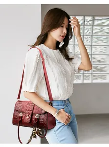 Detail of burgundy crocodile-textured handbag with gold logo and leopard tassel charm
