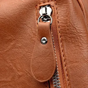 Macro detail of silver metal zipper and teardrop leather pull on brown textured backpack