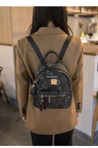 Detail of a black leather mini backpack with white letter print and golden metal logo plate