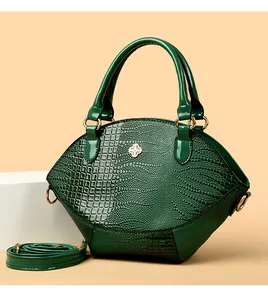 Dettaglio borsa verde scuro con motivo a coccodrillo, logo dorato e manico superiore