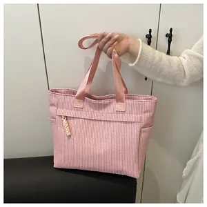 Detail van roze corduroy draagtas met verticale textuur en gele kwastjesversiering
