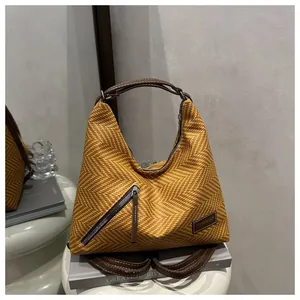 Close-up of yellow herringbone weave bag with brown leather handles and metal zipper detail