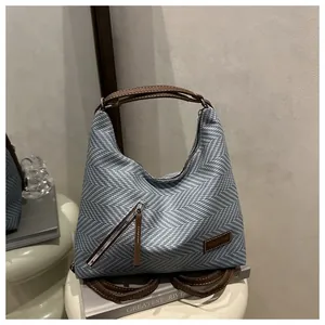 Detail of blue herringbone woven bag featuring brown leather handle and metal zipper accent