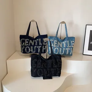 Détail de trois sacs cabas en denim avec lettrage effiloché GENTLE YOUTH en noir et bleu