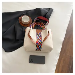 Borsa a mano crema con tracolla etnica colorata e manici marroni su tessuto bianco
