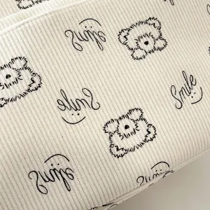 Detailansicht aus cremeweißem Cordstoff mit süßem Bären und Smile-Stickerei