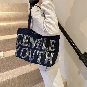 Détail du cabas en denim bleu foncé avec broderie Gentle Youth et bandoulière