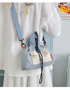 Detail of light blue nylon crossbody bag featuring a beige front pocket and drawstrings
