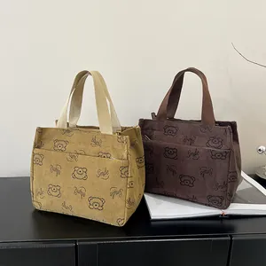 Detailansicht der khakifarbenen und braunen Cord-Lunchpakete mit Bärenmotiven und Smile-Text