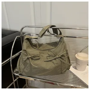 Close-up of olive green crossbody bag with decorative bows on a metal shelf