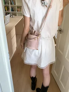 Pink drawstring bucket bag with shoulder strap worn by a woman in a bright studio