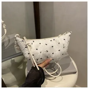 Detail of white pleated dumpling bag with black bow patterns and knotted rope shoulder strap