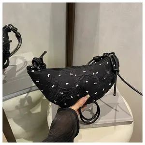 Detail of black pleated crescent bag with white bow embroidery and knotted shoulder strap