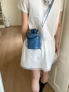 Blue denim texture bucket bag with letter print and gold chain strap on white dress