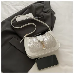 Close-up of beige sequin shoulder bag with golden lock on a grey suit and book
