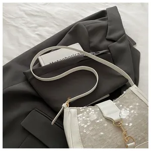 Close-up detail of white sequin and leather stitching with gold metal clasp on bag
