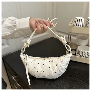 Detailed view of white croissant bag featuring black bow embroidery and knotted rope handle