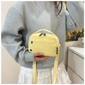 Close-up of light yellow nylon crossbody bag featuring multi-zipper pockets and brand tag