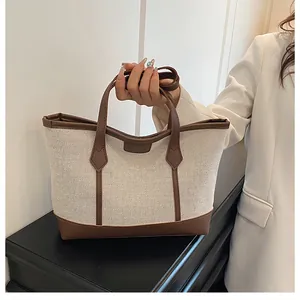 Detail of a contrast stitch tote bag with cream woven fabric and brown leather handles