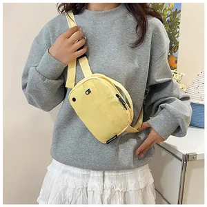 Model wearing a bright yellow nylon crossbody bag with black zipper and adjustable strap