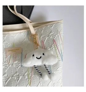 Close-up of a white plush cloud charm with striped legs on an embossed tote bag
