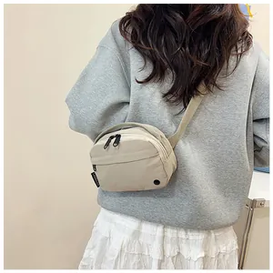 Macro detail of casual beige nylon crossbody bag featuring double zippers and branded side tag
