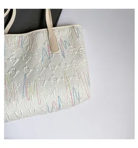 Close-up of quilted cream tote bag featuring colorful wavy embroidery and embossed texture