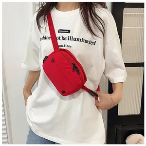 Detailed view of a red nylon crossbody bag with black zippers on a white t-shirt model