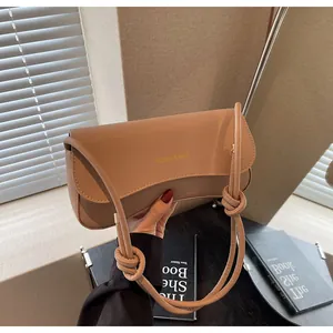 Close-up of khaki leather baguette bag featuring gold lettering and knotted strap detail