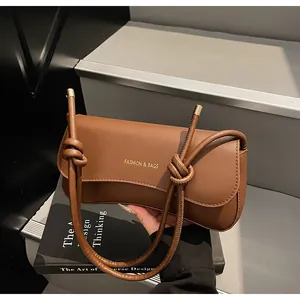 Close-up of dark brown leather underarm bag with gold logo and knotted shoulder strap