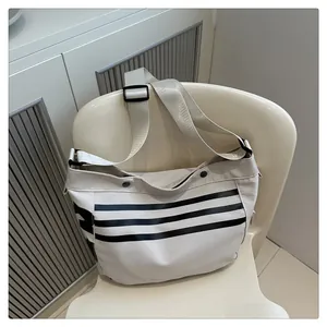 Gros plan du sac bandoulière en nylon crème avec rayures noires et large sangle réglable