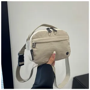 Detail of minimalist beige nylon crossbody bag with adjustable strap and dual zippers