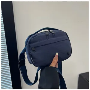 Detail of navy nylon crossbody bag showing multiple zippers and adjustable buckle strap
