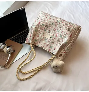 Detail of floral tote bag with braided handles and plush star charm on white bedding