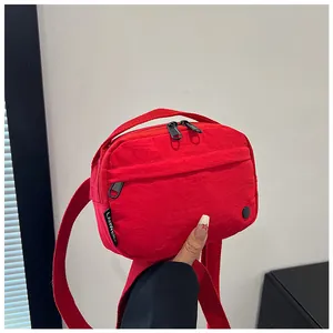 Detailed view of red nylon crossbody bag with black zippers and woven brand label