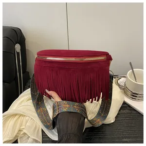 Close-up of burgundy suede crossbody bag with fringe detail and ethnic print strap