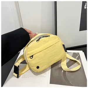 Detail of light yellow nylon crossbody bag featuring black adjustable strap and zippers