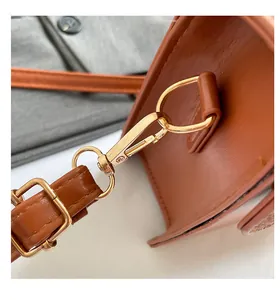 Close-up of brown leather shoulder bag featuring gold lobster clasp and adjustable strap