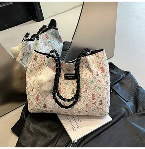 Detail of cream knit tote bag with bear print, black chain strap, and plush charm accessory