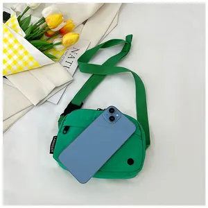 Close-up of bright green nylon crossbody bag with shoulder strap next to a blue phone