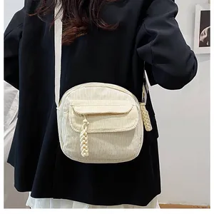 Detail of cream corduroy crossbody bag texture and fabric strap on black blazer