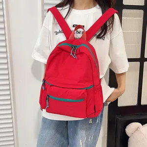 Close-up of red nylon backpack with contrasting blue zippers worn by model in casual setting
