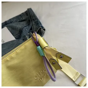 Detailopname van gele crossbodytas met geborduurde letters en geweven touwhanger