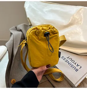 Detail of a ginger yellow nylon crossbody phone bag with drawstring front pocket and strap