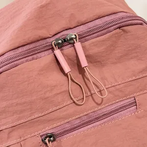 Dettaglio delle doppie cerniere metalliche su uno zaino in nylon viola e rosa