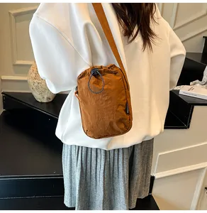 Brown nylon crossbody bag with drawstring design and fashion label on a white sweatshirt