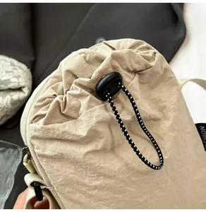 Detail of waterproof nylon crossbody bag featuring beige fabric and black drawstring closure